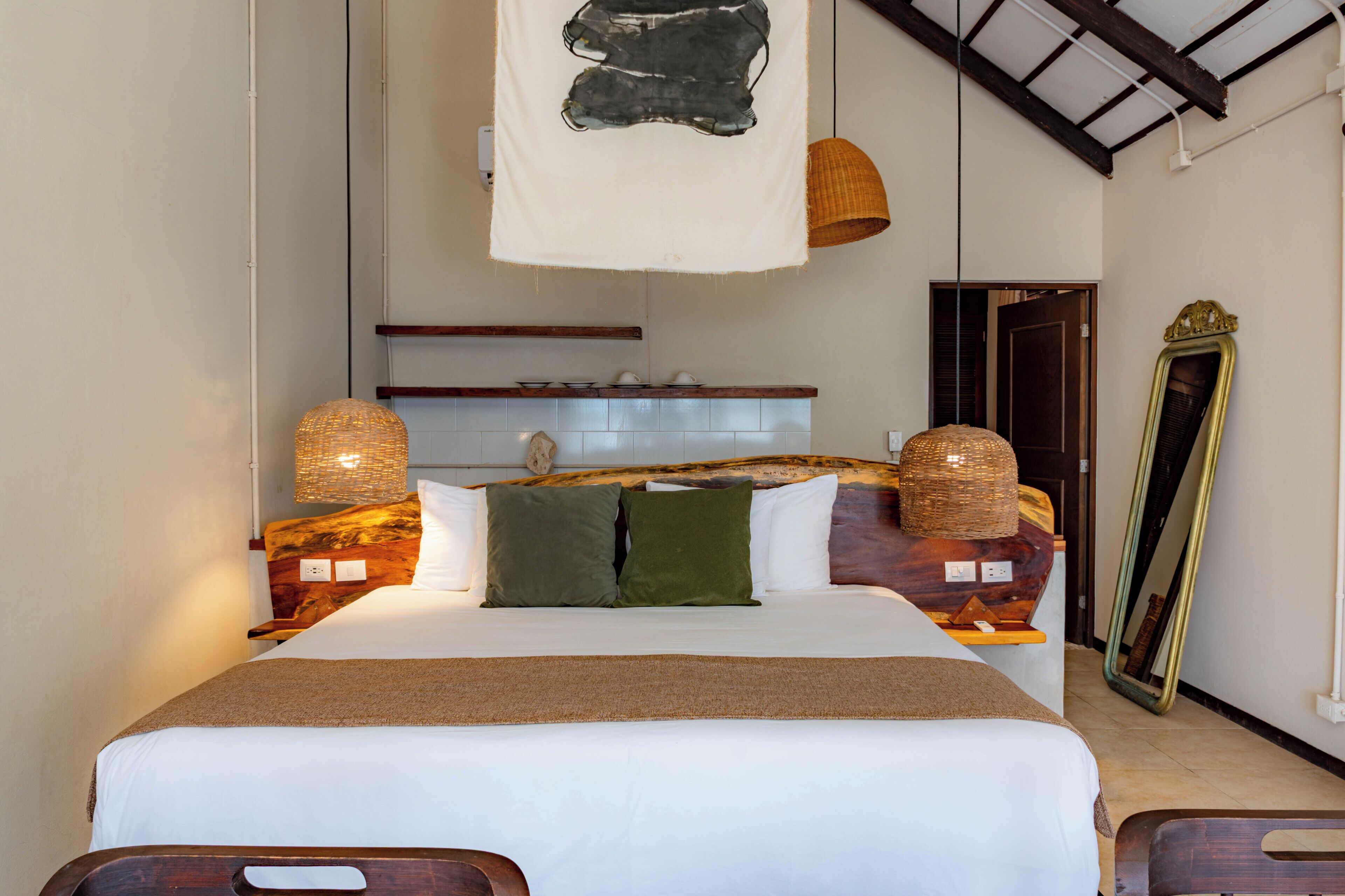 A bedroom with a bed, pillows, a headboard, a hanging light, a mirror, and a wooden headboard.
