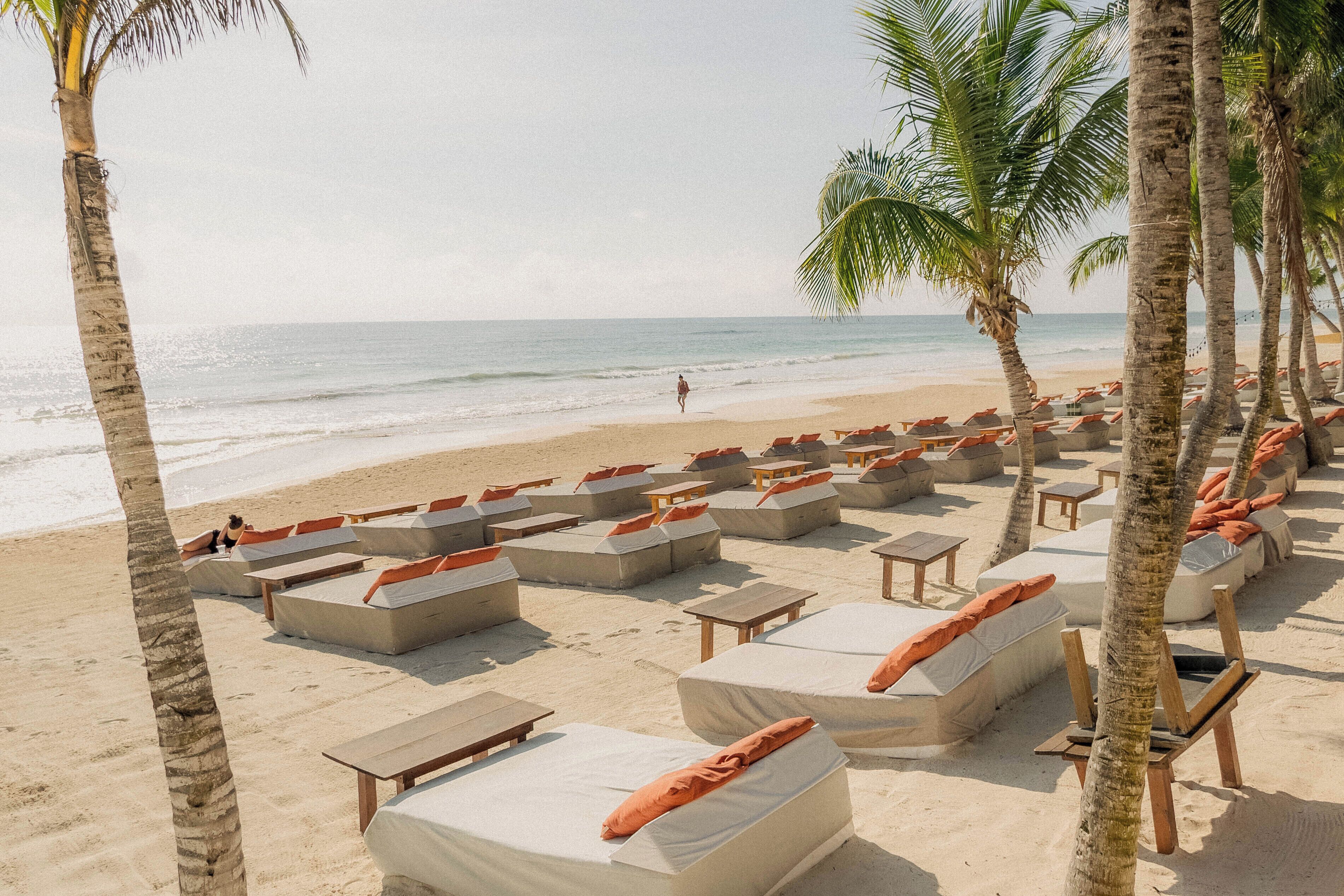 A beachside lounge area with multiple seating options, including sofas and benches, arranged in rows facing the ocean.