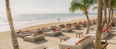 A beachside lounge area with multiple seating options, including sofas and benches, arranged in rows facing the ocean.