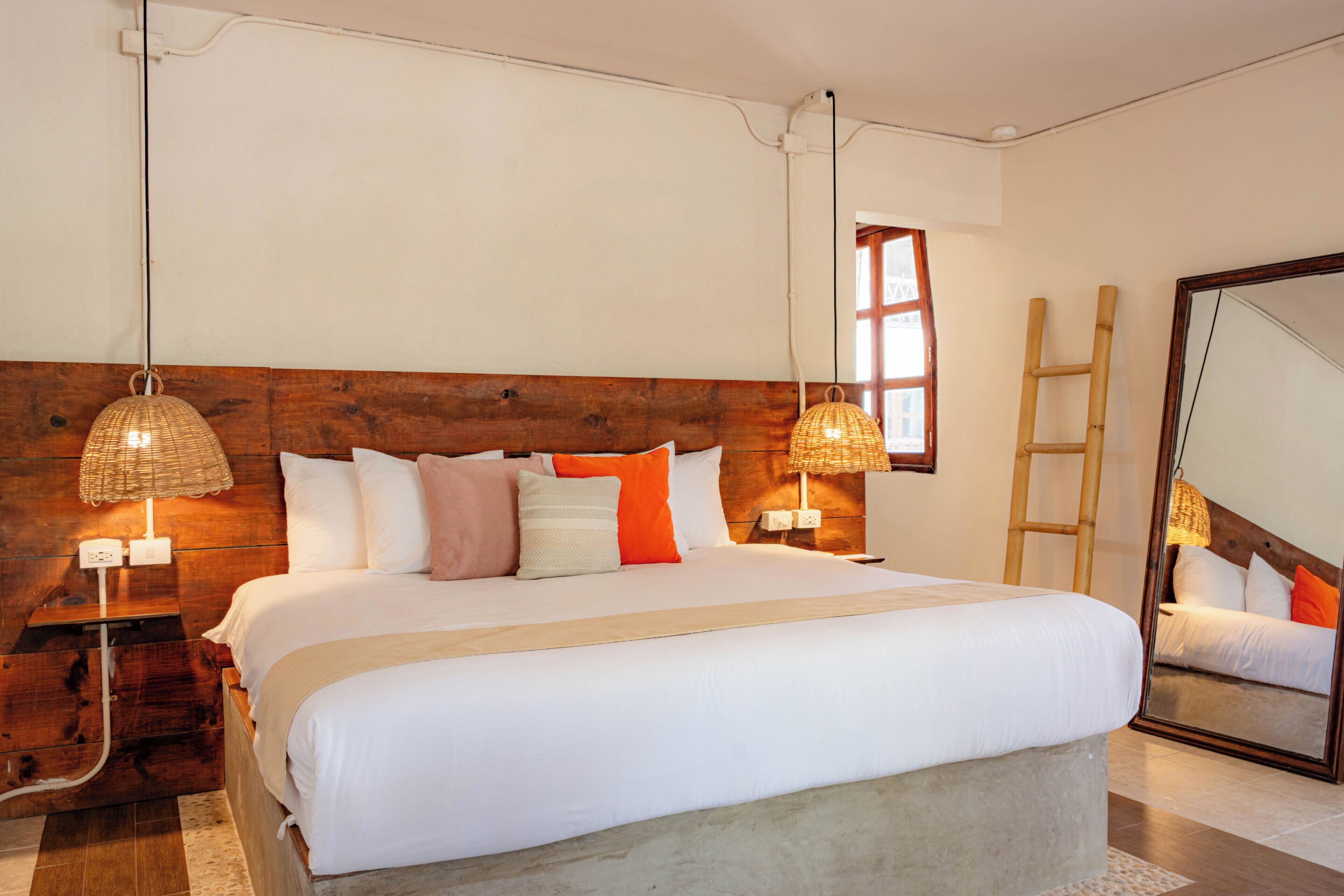 A bedroom with a large bed, wooden headboard, bedside lamps, a ladder, and a mirror.