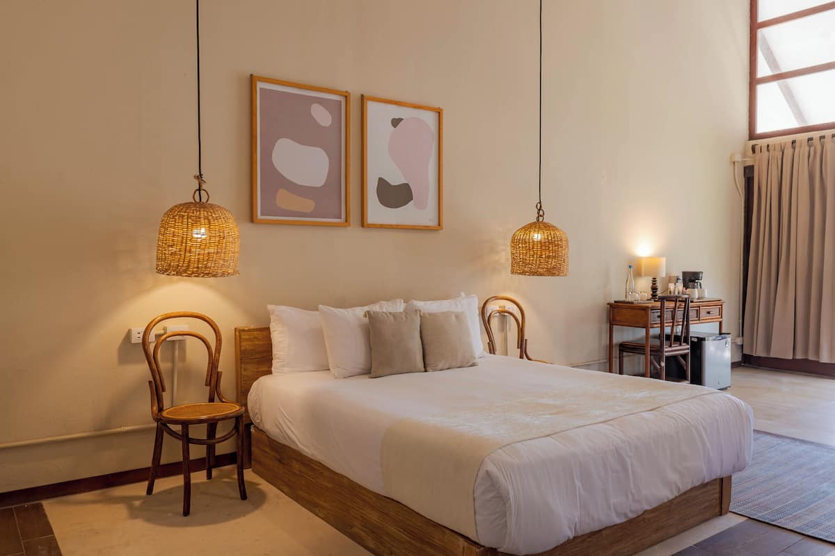 A neatly arranged bedroom with a bed, two chairs, a desk, and two wall-mounted lamps.