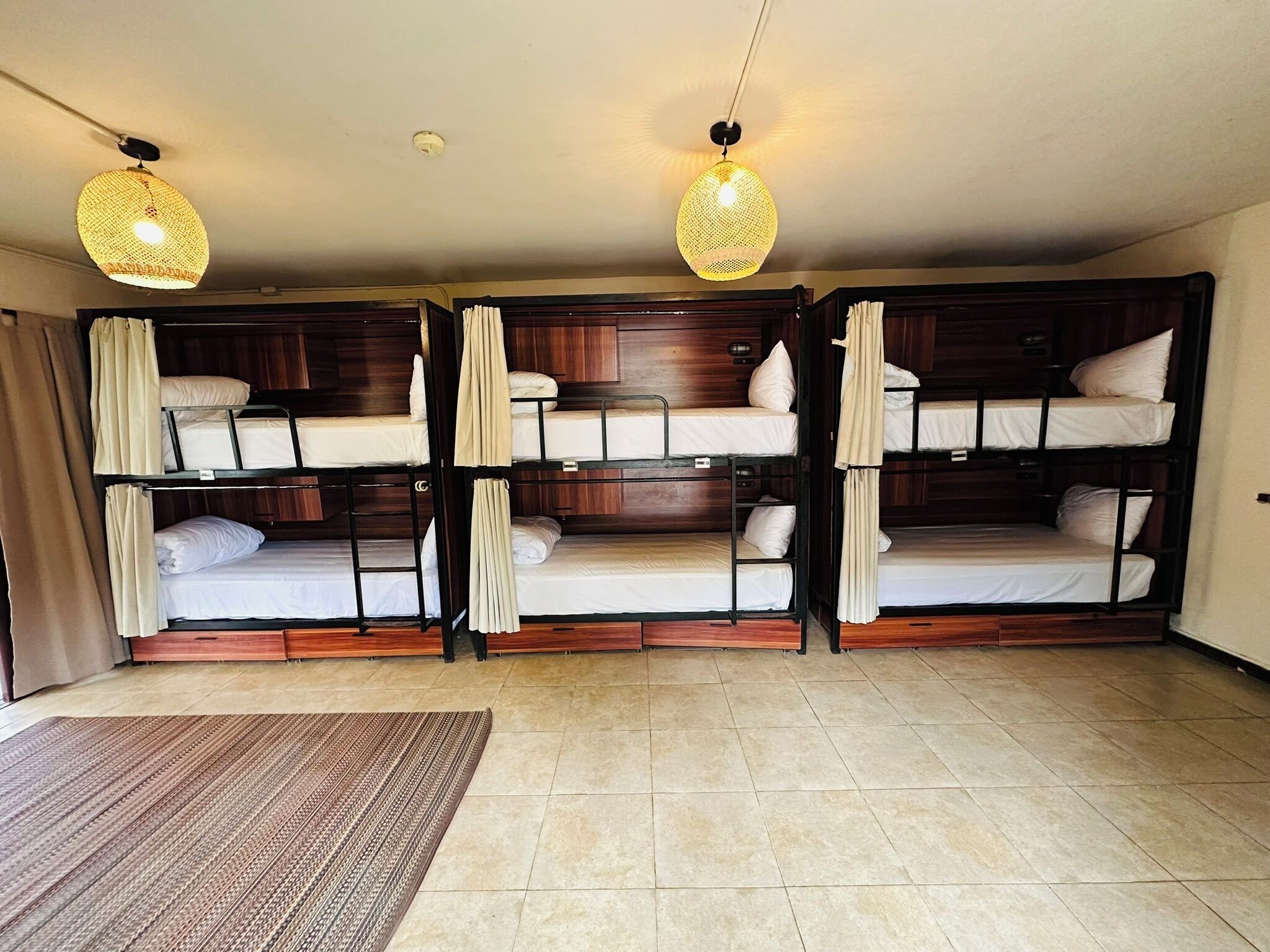 A room with three bunk beds, a wooden floor, and two hanging lamps.