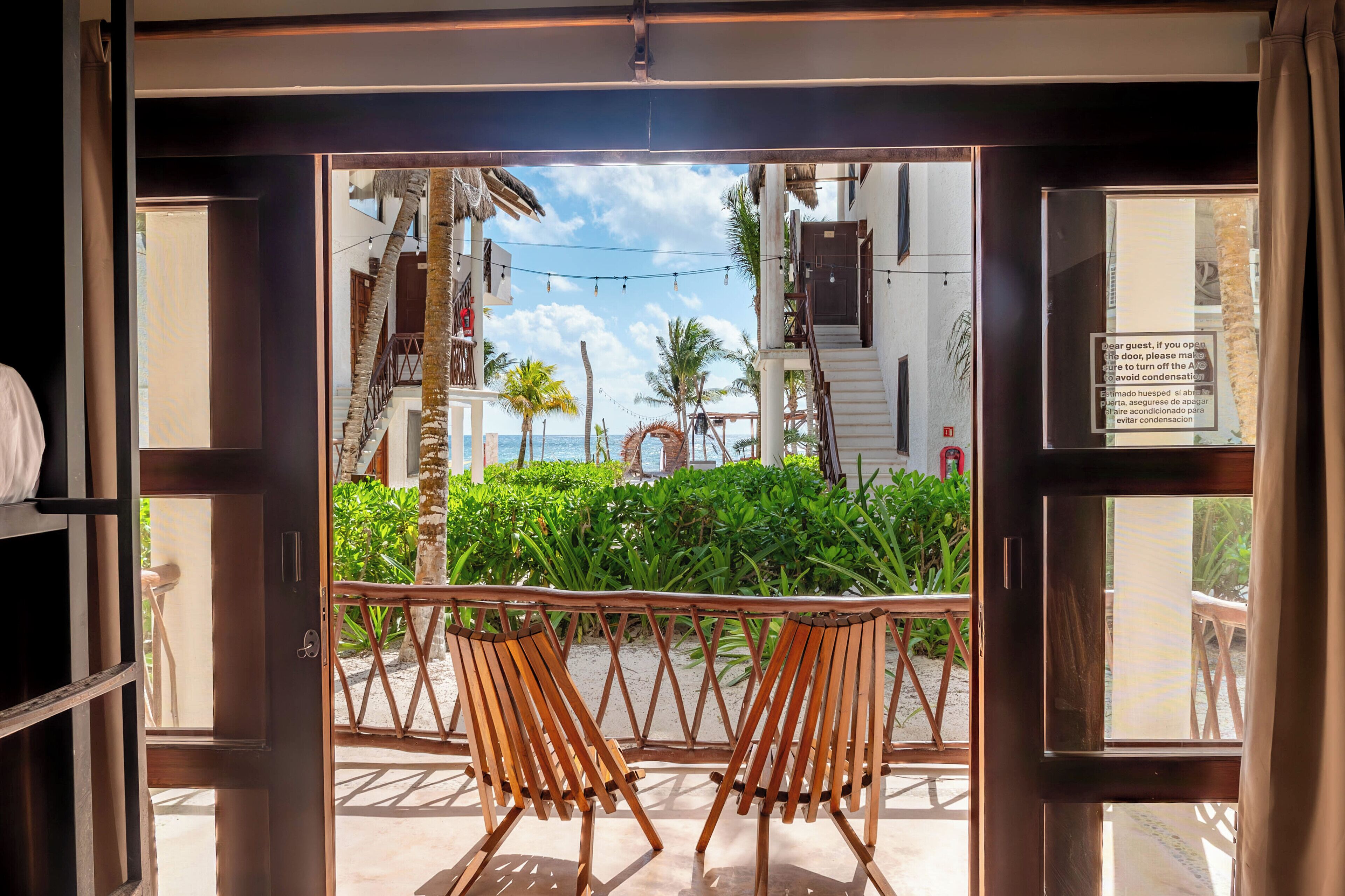 A view from a room with a wooden door leading to an outdoor area with chairs and a table, a staircase, and a sign with instructions.