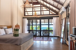 Un dormitorio con una cama grande, vista al océano y un balcón con sillas de madera.