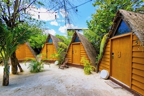 A row of wooden cabins with thatched roofs, each with a door and a window, surrounded by palm trees and sand. - Mía Tulum Beachfront Resort - Ocean View Suites and Beach Club (Tulum)