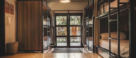 A hotel room with bunk beds, a wooden wardrobe, a woven light fixture, and a view through a glass door.