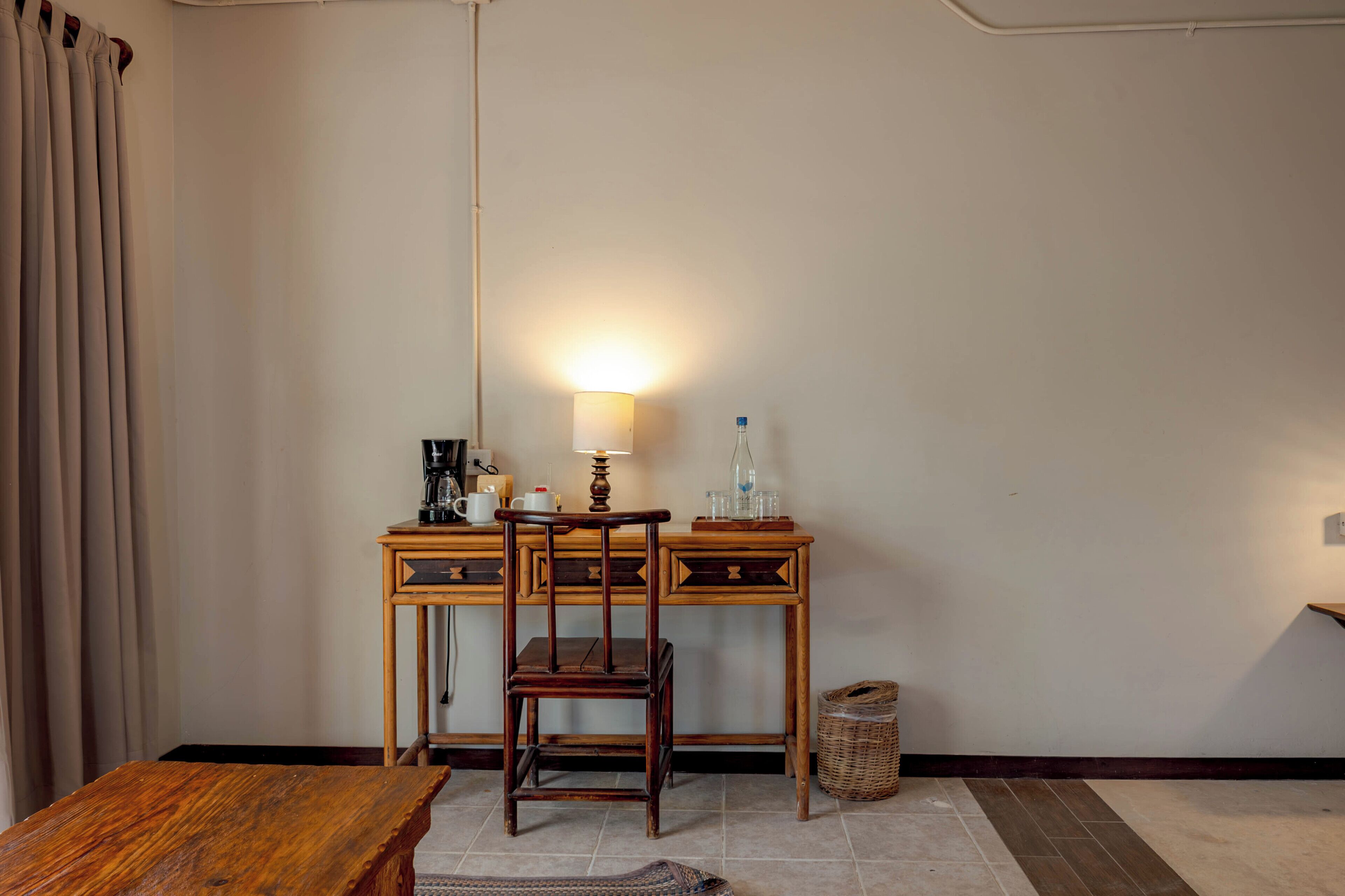 Ein Zimmer mit einem Holztisch, einem Stuhl, einer Lampe und einem kleinen Tisch.