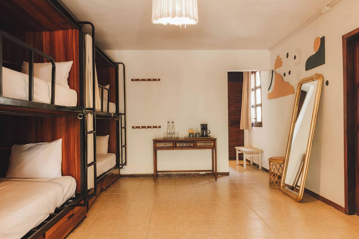 A room with bunk beds, a small table with bottles, a mirror, and a bench.