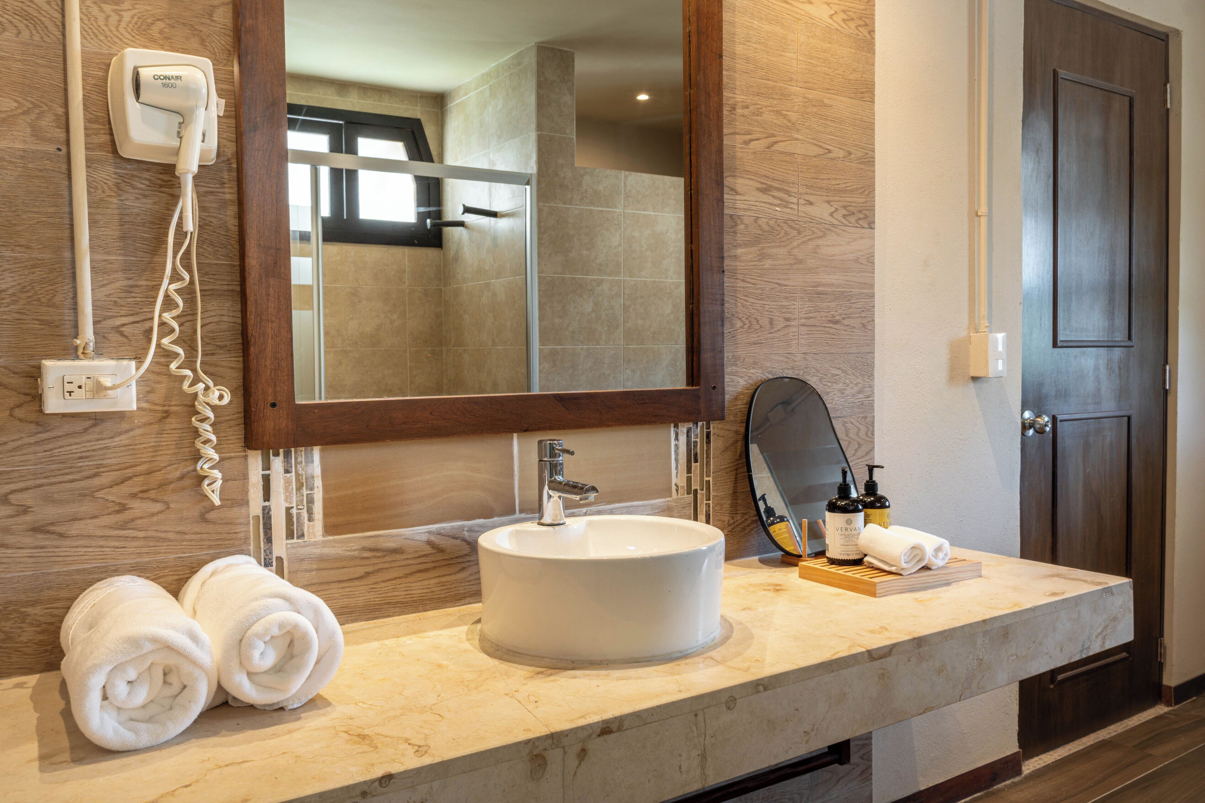A bathroom with a round sink, a mirror, a towel rack, and a door.