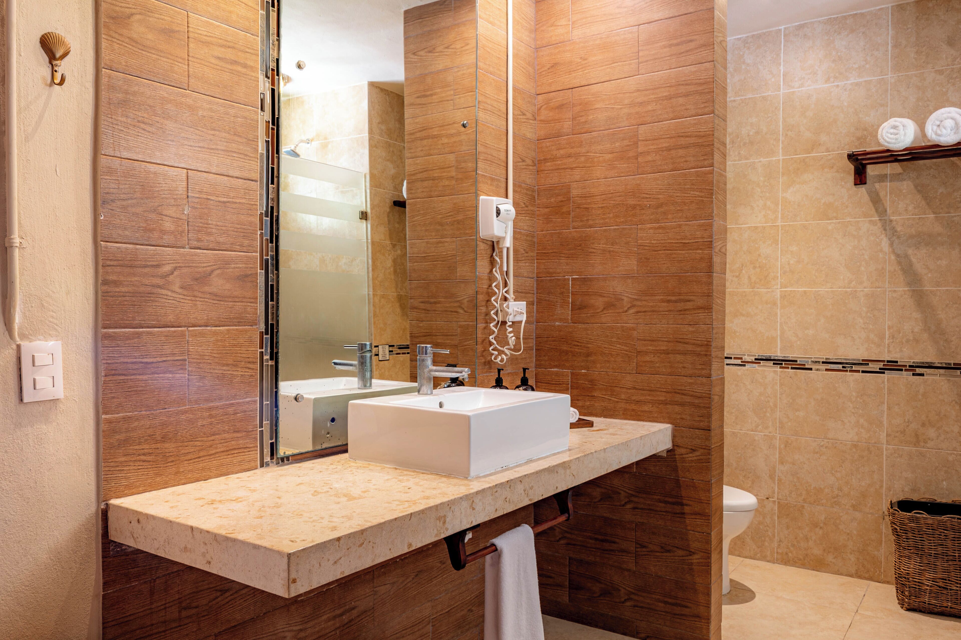 Un baño con tocador de madera, un lavabo blanco, un espejo, un perchero para toallas y un inodoro.