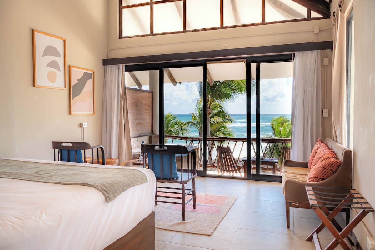 A bedroom with a bed, a desk, a chair, and a balcony with a view of the ocean.