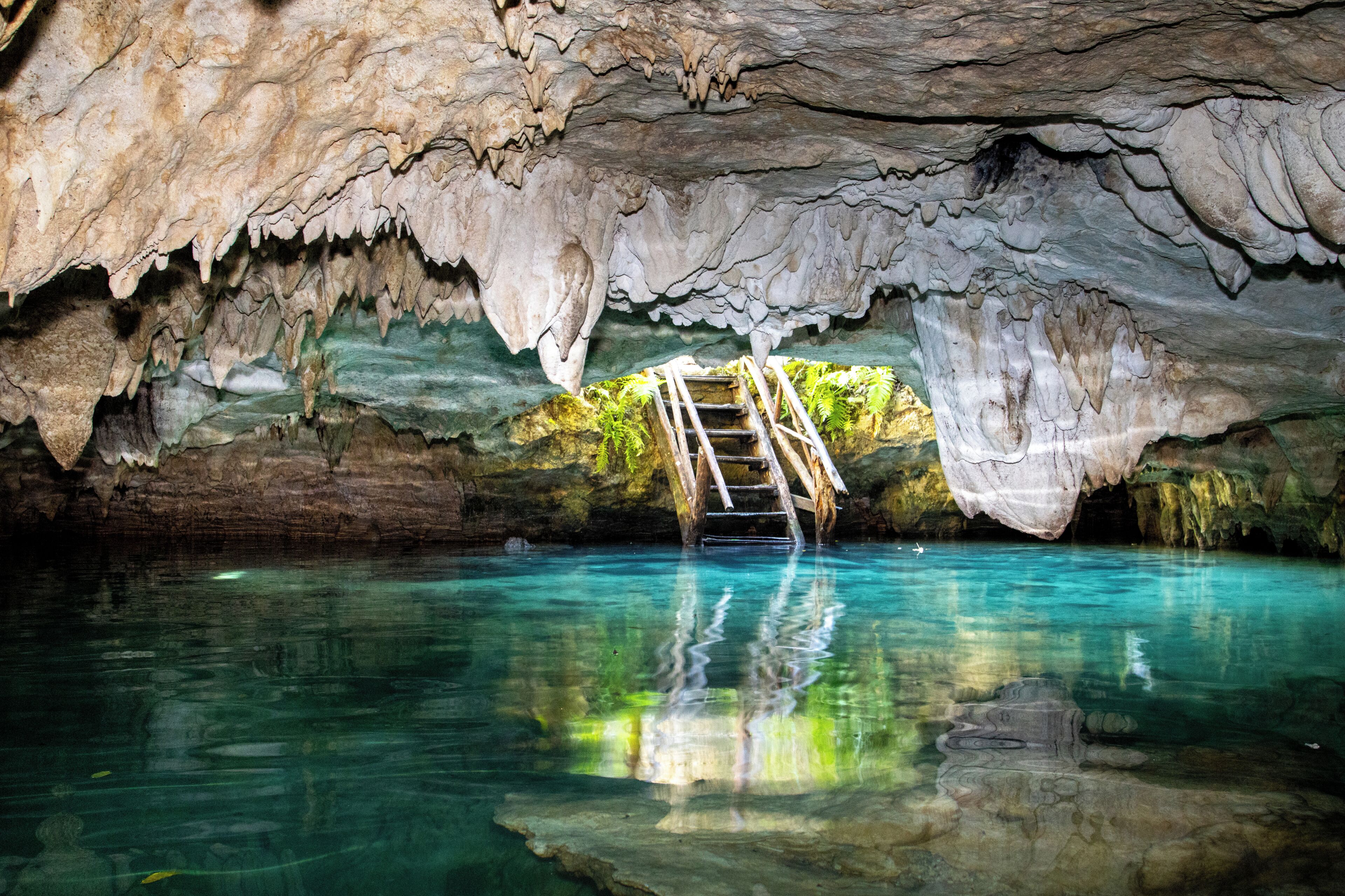 Uma caverna com estalactites, uma escada de madeira e água cristalina.
