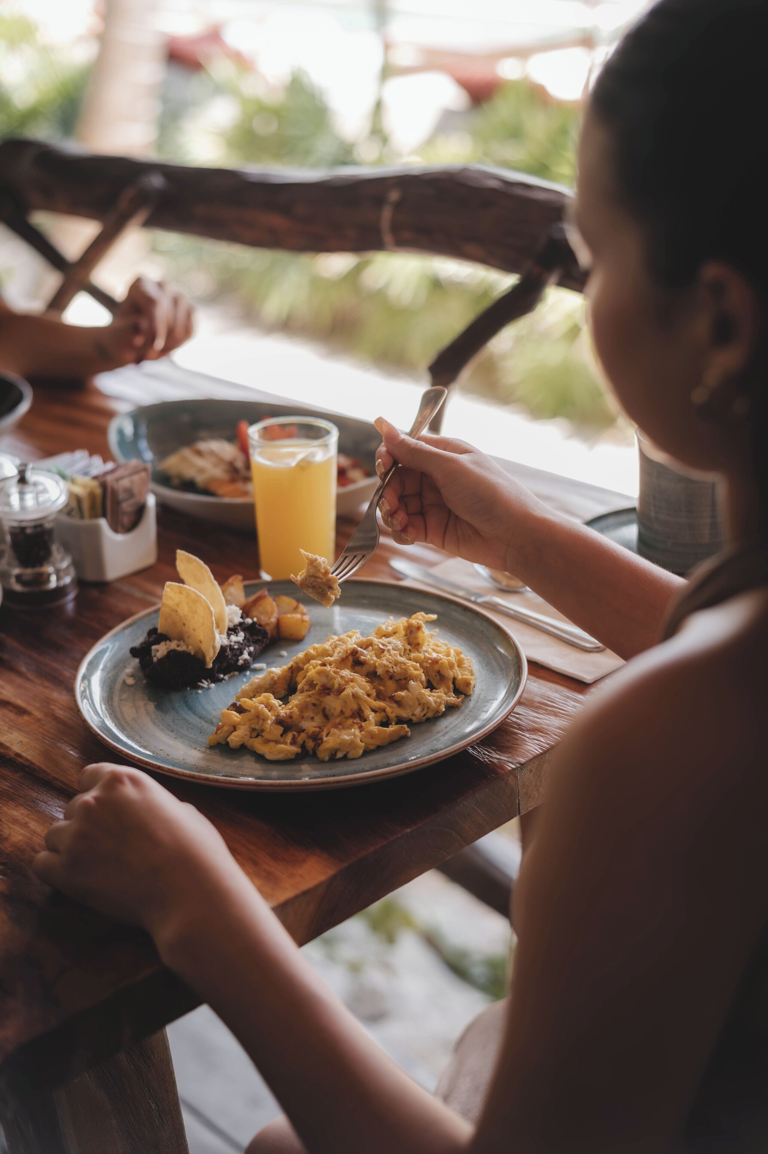 A wooden dining table with a plate of food, a glass of orange juice, and a salt shaker.