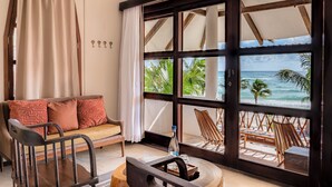 A room with a sofa, chairs, a window with a view of the beach, and a bottle on a table. - Mia Tulum Beachfront Resort - Ocean View Suites and Beach Club (Tulum)