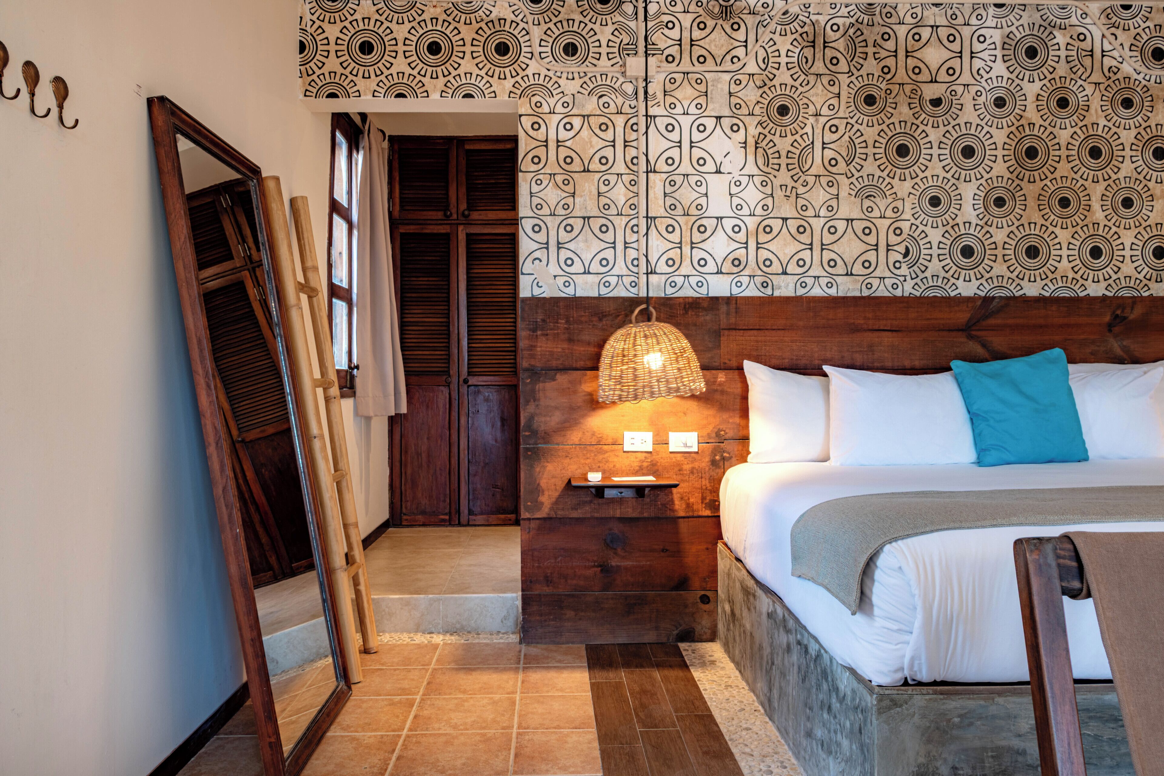 A bedroom with a bed, a nightstand, a lamp, a mirror, and a patterned wall.