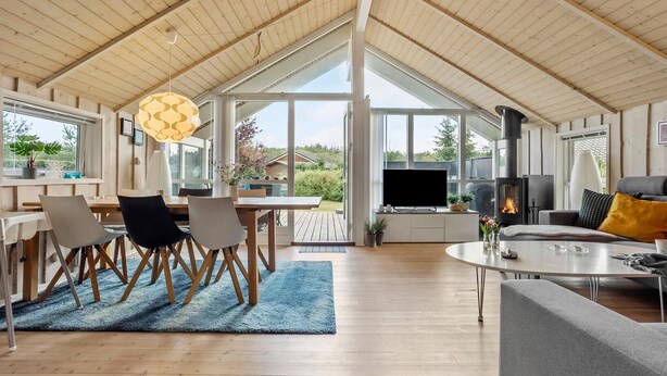 A spacious living area with a high ceiling, wooden beams, a fireplace, and a large window overlooking a garden. - Gorgeous home in Ebeltoft with sauna (Ebeltoft)
