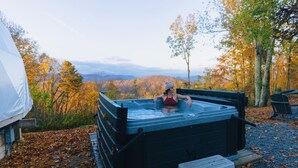 Vasca idromassaggio in un ambiente naturale con vista su alberi autunnali e montagne.