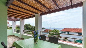 Un balcon avec une table et des chaises, une vue sur la mer et des bâtiments en arrière-plan.