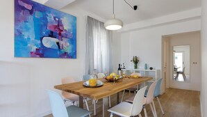 Un coin repas avec une table en bois, des chaises bleu clair et un tableau abstrait aux couleurs vives accroché au mur.