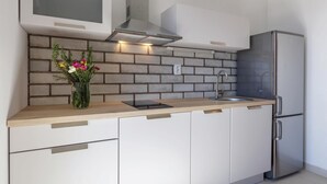 Une cuisine moderne équipée d’un réfrigérateur en acier inoxydable, d’un four à micro-ondes encastré et d’une hotte aspirante. On y trouve un plan de travail en bois, un évier et un vase de fleurs.