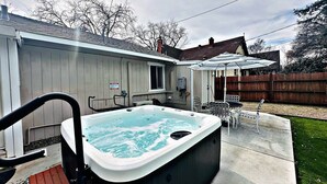 A hot tub in a backyard with a wooden deck, a patio table, and chairs. - Jacuzzi Delight - Luxe 2BD/2BA near UC Davis Med (Sacramento)