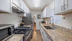 A kitchen with white cabinets, a stainless steel range, a microwave, and a granite countertop. - Jacuzzi Delight - Luxe 2BD/2BA near UC Davis Med (Sacramento)