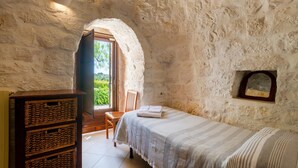 A rustic stone room with a bed, a wooden cabinet, and a door leading outside. - 3 bedroom cozy home in Ostuni (Ostuni)