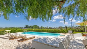 A swimming pool with lounge chairs and a sunbed, surrounded by greenery and a clear sky. - 3 bedroom cozy home in Ostuni (Ostuni)