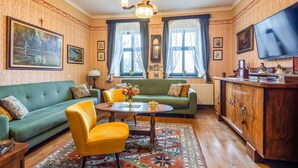Un salon chaleureux avec un canapé vert, un fauteuil jaune, un meuble en bois et un téléviseur placé à droite.