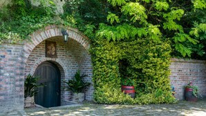 Une arche en briques surmontée d’une porte en bois, d’une lanterne et de plantes en pot.