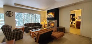 Relax by the fireplace in this inviting living room with a view of snow-covered trees.
