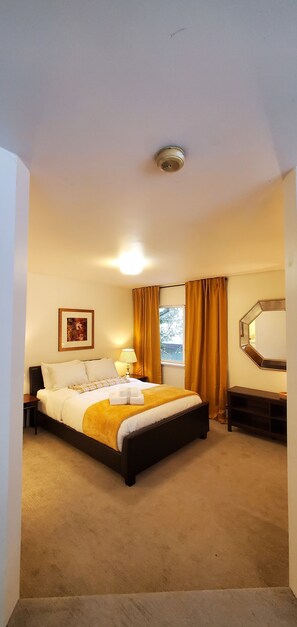 Relax in comfort with a large bed, nightstand, and lamp, plus a window with curtains and a framed picture on the wall.