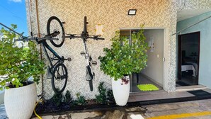 A building with a textured wall, a bike rack with two bicycles, and two large potted plants. - Pousada Cantinho de Piri (Pirenópolis)