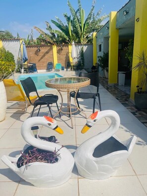 Un espace aménagé au bord de la piscine, avec une table ronde, des chaises et deux fauteuils de relaxation en forme de cygne.