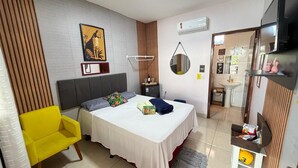 A hotel room with a bed, a chair, a mirror, a shelf with items, and a wall-mounted air conditioner. - Pousada Cantinho de Piri (Pirenópolis)