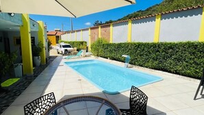 A pool area with a glass table and chairs, surrounded by a tiled patio and a white wall with yellow accents. - Pousada Cantinho de Piri (Pirenópolis)