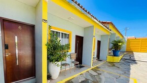 A building with numbered doors, a covered outdoor seating area with chairs, and potted plants. - Pousada Cantinho de Piri (Pirenópolis)