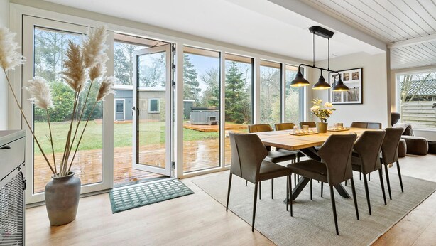 A modern dining area with a large table, chairs, and a view of the backyard through glass doors. - 4 bedroom stunning home in Væggerløse (Væggerløse)