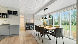 A modern kitchen with a built-in oven, a dining area with a wooden table and chairs, and large windows offering a view of the outdoors. - 4 bedroom stunning home in Væggerløse (Væggerløse)