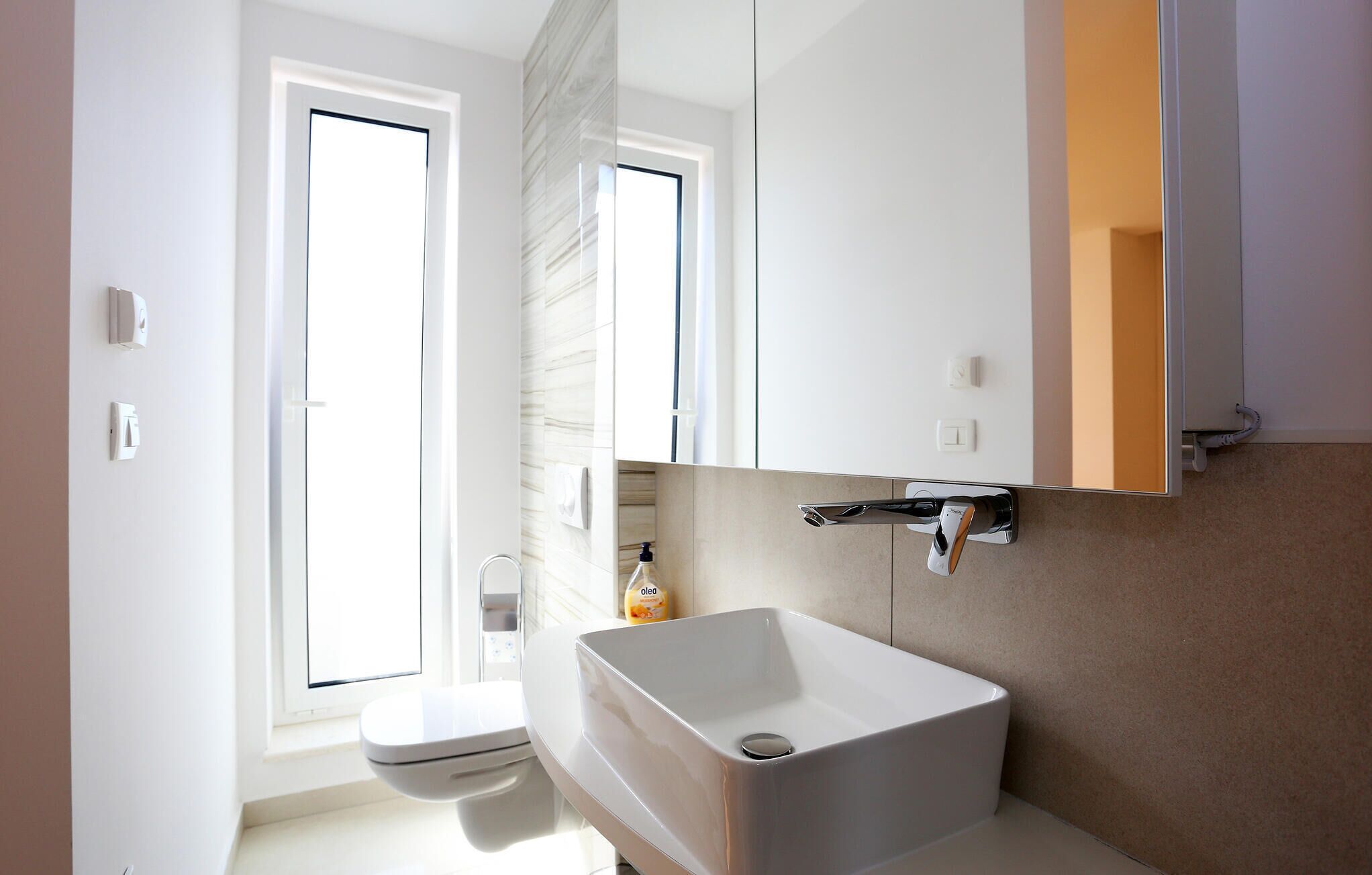Ein modernes Badezimmer mit einem weißen Waschbecken, einer Toilette und einem Spiegel über dem Waschbecken.