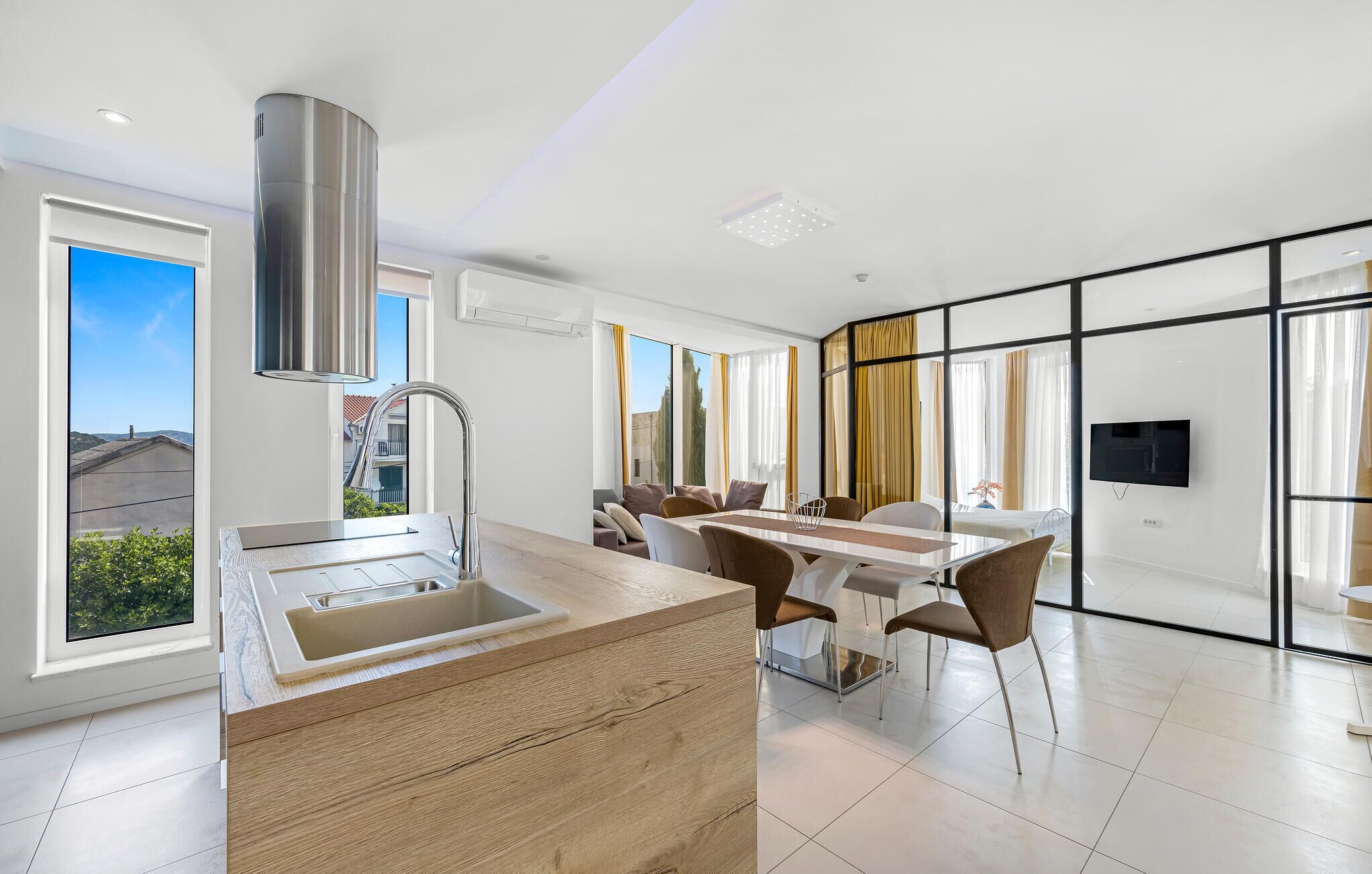 A modern kitchen with a large island, a dining area with a table and chairs, and a TV mounted on the wall.