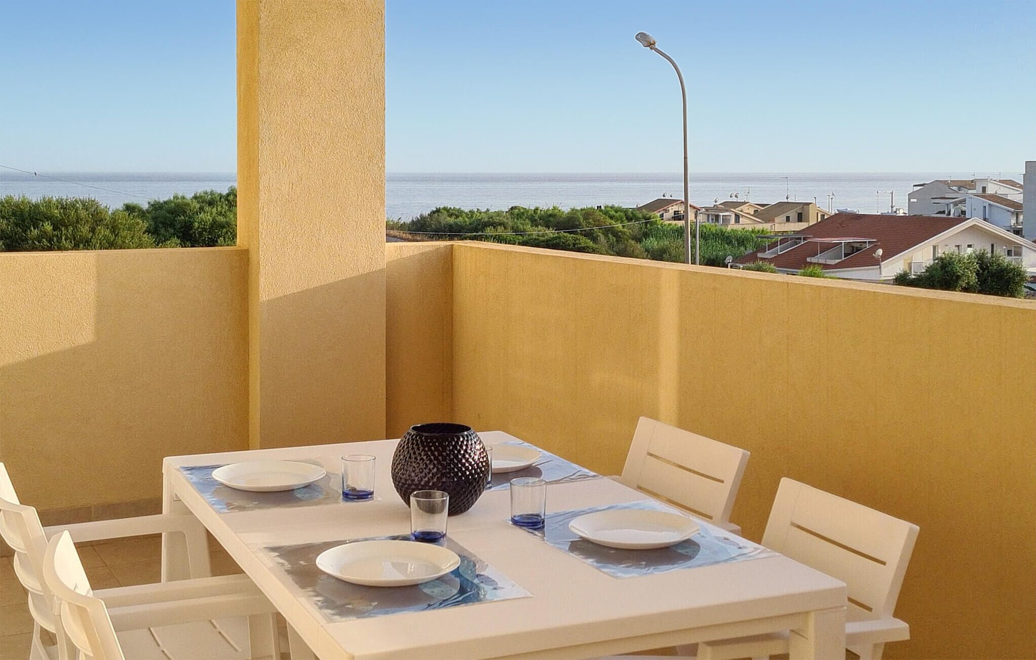Ein Balkon mit Tisch für zwei Personen, mit Blick auf die Küste und Häuser im Hintergrund.