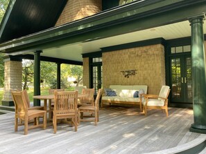 A covered patio area with a brick wall, wooden furniture, and a green column.