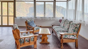 Habitación con muebles de madera, incluyendo un sofá y sillas, y vistas a colinas a través de amplias ventanas.