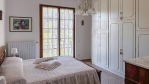 Un dormitorio con una cama grande, un radiador, una ventana con cortinas, una lámpara de araña y un armario.