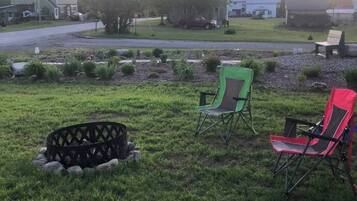 A grassy outdoor area with a fire pit, two folding chairs, and a bench.