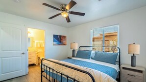 Ein Schlafzimmer mit Bett, Nachttischen, Deckenventilator, Fenster mit Jalousien und einer Tür.