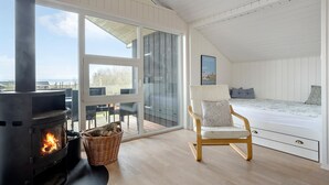 Una habitación acogedora con una estufa de leña, una cesta de mimbre, una silla de madera y una cama con almohadas.