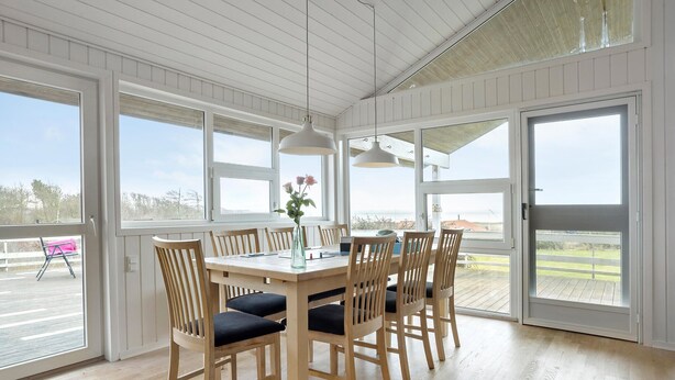 Un comedor con mesa y sillas de madera, ventanas amplias y vistas al exterior.