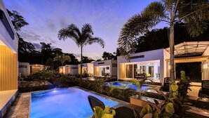 Un área de piscina con varias piscinas, sillas de descanso y palmeras.